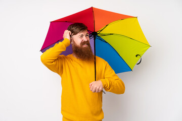 Redhead man with long beard holding an umbrella over isolated white background having doubts and...