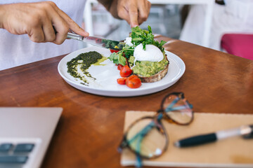 Cropped image of male eating healthy food for lunch with green guacamole on brusquet, tasty delicious toast with green vegan snack for lunch with tomatoes and egg