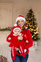 Happy mother hug little daughter in red Santas costume and hat, near Christmas tree