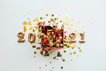 Festive gift box with ribbons. In the background are numbers 2021 and confetti. New Year and Christmas conceptual background.