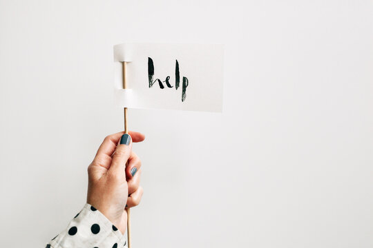 woman holding a white paper flag with ""help"" written on it