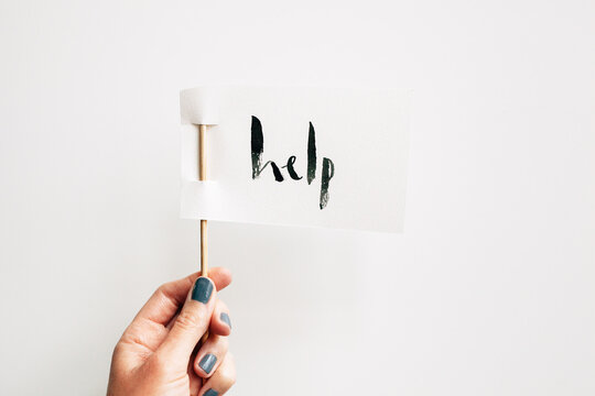 hand holding a white paper flag with ""help"" written on it