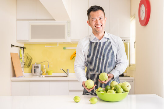 Young man holding guava fruit in kitchen.