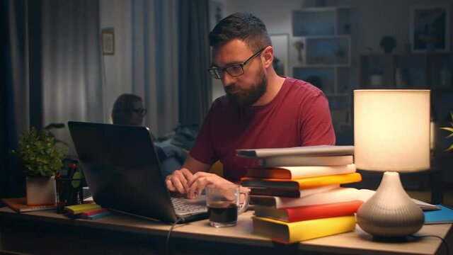 Young man typing on laptop at home in living room at his desk