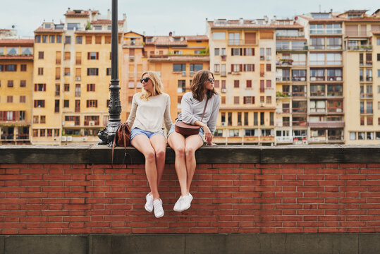 Two tourist girl friends relaxing on historical bridge in Floren