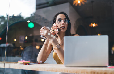 Thoughtful woman with coffee and laptop talking on phone