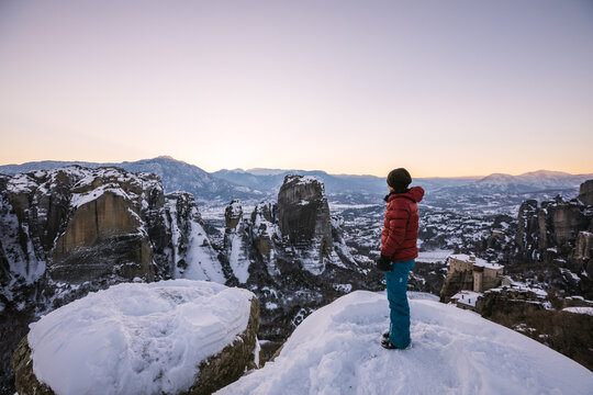 woman standing on the edge of snowcovered rocks overlooking the beautiful landscape of meteora