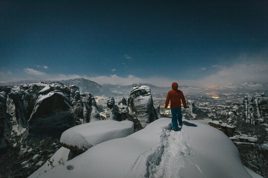 male mountaineer standing on snowcovered rocks overlooking meteora at night