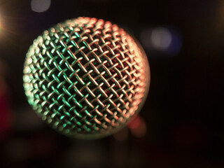 Microphone on stage with red and green light reflecting on the grid, ready to be used (closeup)
