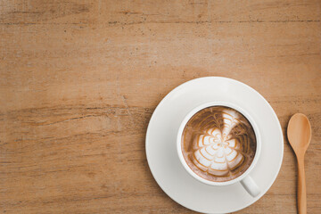 hot latte coffee and bubble in white coffee cup and saucer with spoon on wooden background.top view,flat lay,top down.