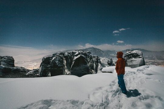 male mountaineer overlooking snowcovered meteora at night