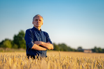 Selective focus on man standing in rape wheat field. Harvest season. Male stands cross hands against blue sky.