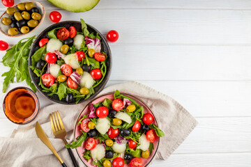 Two servings of fresh vegetable salad - tomatoes, lettuce, olives, arugula and olive oil. Top view, copy space