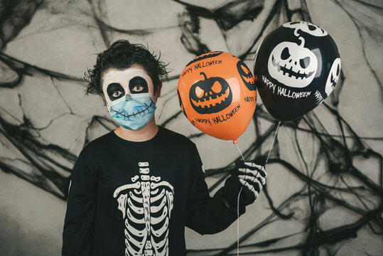 Happy Halloween. kid with medical mask in a skeleton costume with halloween balloons