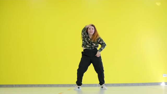 Young energetic woman dancing modern youth dance free style in the studio against the background of a yellow wall. Isolated.