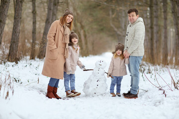 Fototapeta na wymiar a family with young daughters play in the winter forest and make a snowman. walking in any weather. new year vacations. happy childhood.