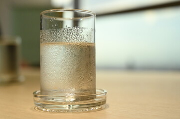 The Plain water with which the ice melted completely was in a clear glass with water droplets attached to it. Place it on a wooden table in a conference room and have a blurred background.
