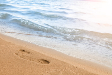 Close-up of the beach shore with a man's footprint on the yellow sand along the line of the blue sea wave on a summer sunny day. Background for advertising travel or tourist vacation.