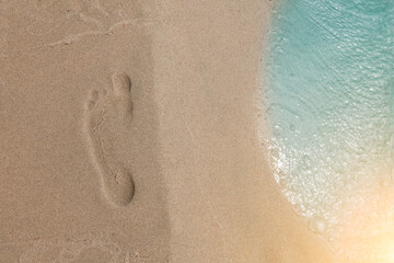 Footprint of a man on a sandy beach top view next to the coastline and turquoise sea water. Background for banner or tourist brochure or advertisement.