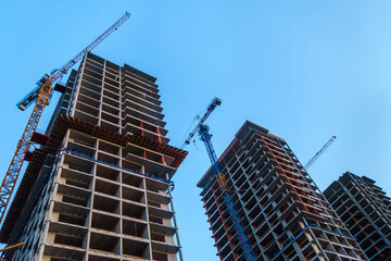 A complex of high-rise buildings under construction and cranes at each of them, bottom up view