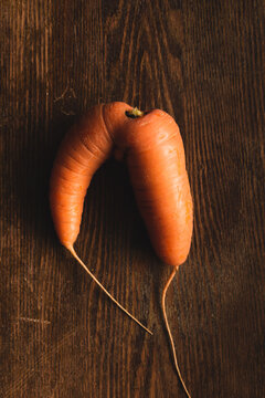 Ugly carrot on a wooden background. Funny, unnormal vegetable or food waste concept. Horizontal orientation
