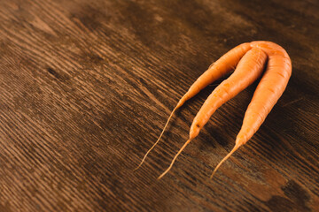 Ugly carrot on a wooden background. Funny, unnormal vegetable or food waste concept. Horizontal...