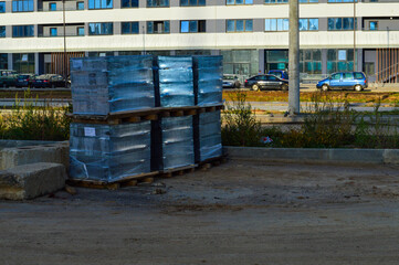 the construction site is packed with material for the construction of new houses in the city. building material in a transparent thick film, on wooden pallets, stands on sandy ground