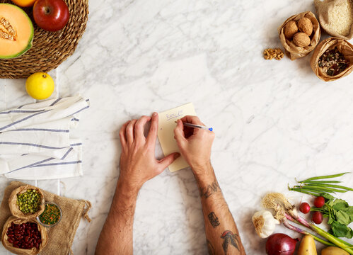 Tattooed man taking notes over marble table with food