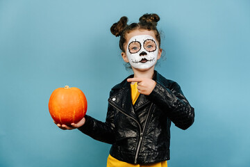 Little preschool girl point finger at orange pumpkin, wears frightening makeup, celebrates...