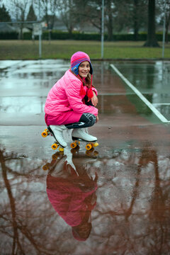 Preteen girl wearing roller skates crouches next to rain puddle on tennis court