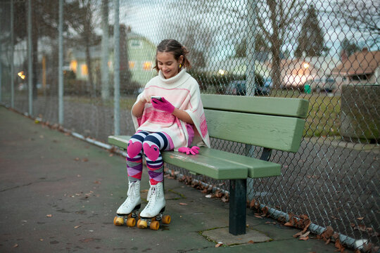 Preteen girl wearing roller skates using smartphone while seated on a bench in the park