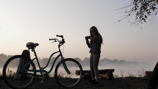 A woman films a vintage bicycle on her smartphone beside a foggy lake at dawn. High quality 4k footage