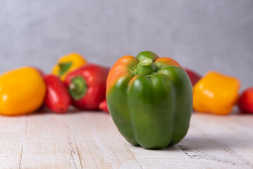unripe bell peppers on a white wooden table with colorful vegetables in the background