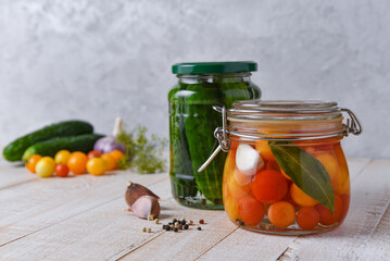 pickled cucumbers and tomatoes in jars on a white wooden table with fresh vegetables in the background