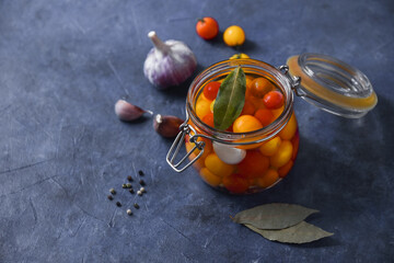 pickled cherry tomatoes in a glass jar on a blue background with garlic and spices