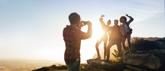 Man photographing his friends on mountain top - obrazy, fototapety, plakaty