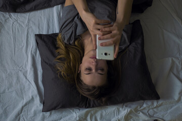Young woman with phone in bed