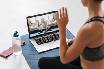 Close up of young fit woman coach in sportswear conducting online fitness training or virtual yoga class on a video conference with laptop. Home workout training. Health practice and wellness concept  - obrazy, fototapety, plakaty