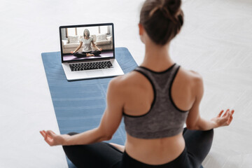 Close up of young sporty woman practicing yoga online with laptop at home. Yoga instructor...