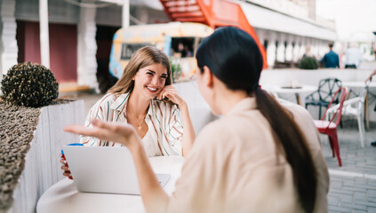 Cheerful young female friends chatting on terrace of modern cafe