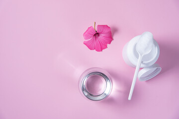 collagen powder with glass of water on pink background in top view