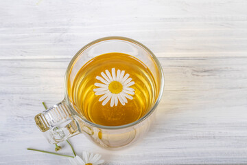 White wooden background in retro style. On it is a glass mug in which chamomile tea is brewed. Copy space. text.