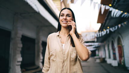Smiling woman answering call on smartphone while standing on empty street