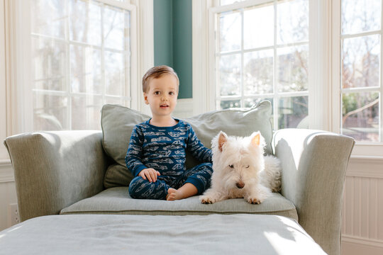 Cute young boy sitting on a large chair petting his dog