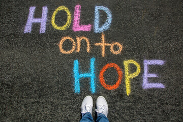 Person standing above a chalk message that says Hold on to Hope