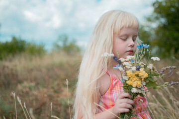 Little girl in nature with a bouquet of wildflowers. Long white hair and pink dress