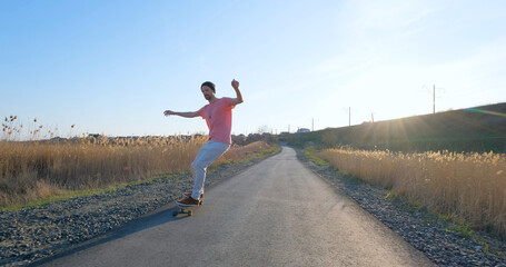 Young male ride on longboard skateboard on the country road in sunny day	