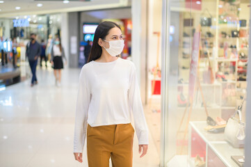 Woman wearing protective mask shopping under Covid-19 pandemic in shopping mall, social distancing protocol, New normal concept.