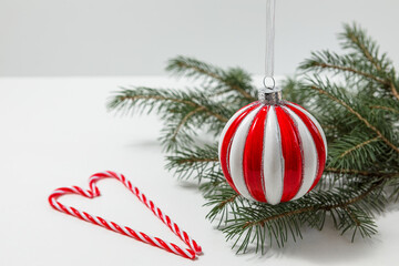 Creative, Christmas and new year, festive composition. striped glass red-and-white ball on the background of a spruce branch on a white table. copy space. selective focus