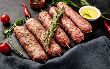 raw Lula kebab  on skewers with spices on a stone background 